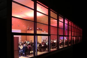 Menschen an festlich dekorierten runden Tischen in abendlicher Lichtstimmung im Seefoyer im Festspielhaus Bregenz