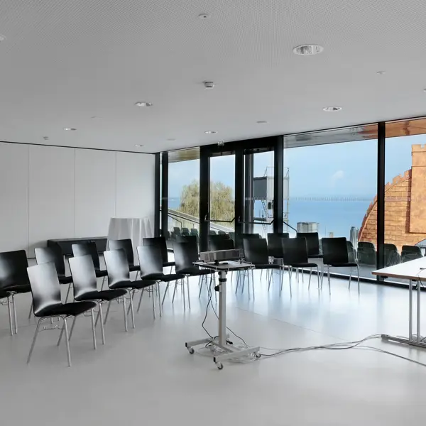 Zwei Stuhlreichen mit schwarzen Stühlen und ein Beamer in der weißen Seegalerie im Festspielhaus Bregenz mit Seeblick © Anja Koehler