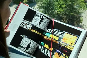 Eine junge Frau liest im Festspielbuch mit Blick auf den Vorplatz des Festspielhauses Bregenz © Kristina Fink