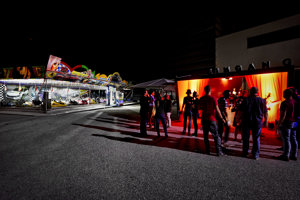 Tagungsteilnehmer:innen amüsieren sich auf dem Vorplatz der Werkstattbühne vor einem bunt beleuchteten Autodrom