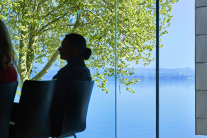 Die Silhouette einer sitzenden Frau vor der Glasfront im Seestudio im Festspielhaus Bregenz mit Blick auf den Bodensee