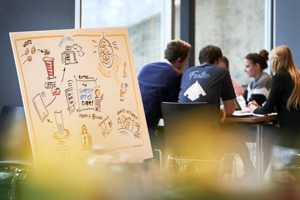 Ein Flipchart im Vordergrund, dahinter sitzen Teilnehmer:innen an einem Tisch im Festspielhaus Bregenz