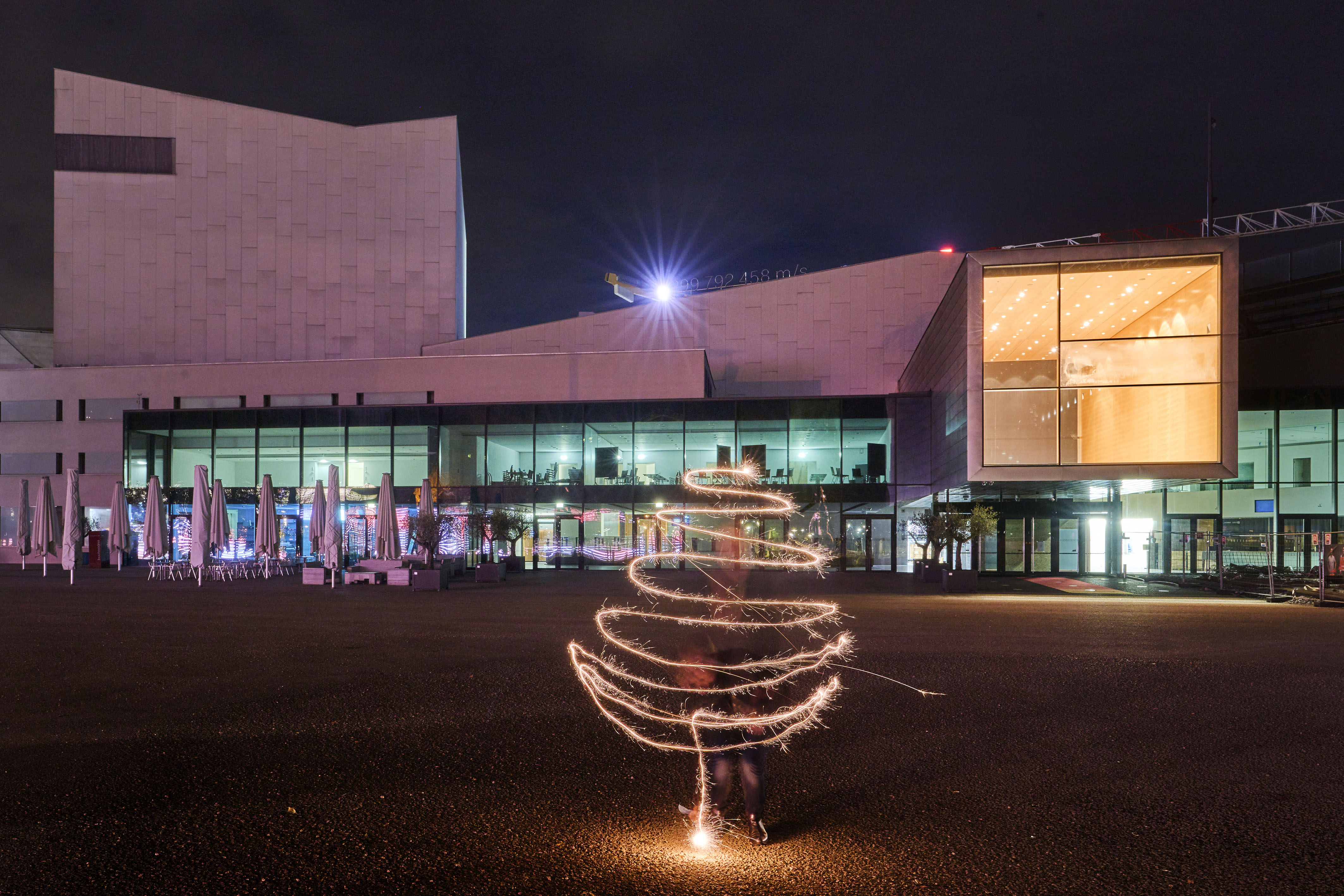 Eine Person zeichnet vor dem Festspielhaus Bregenz mit einer Wunderkerze die Silhouette eines Weihnachtsbaumes © Anja Koehler